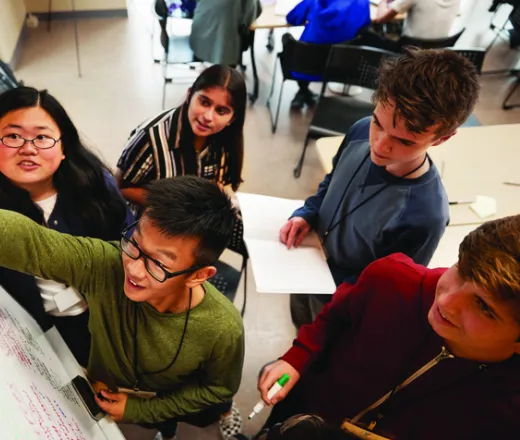 A group of teens gather around a white board to solve an equation